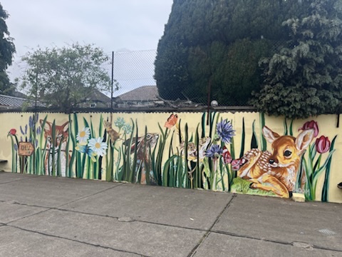 A long outdoor wall mural of a fawn lying among flowers and butterflies