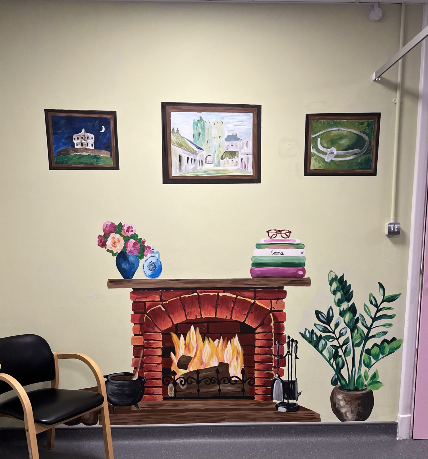 An indoor mural of a cosy brick fireplace, flowers, books and plants