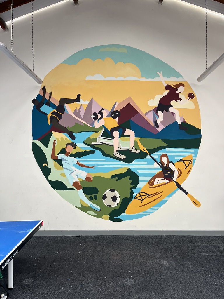 A large circular indoor mural showing children doing sports, mountains and a river