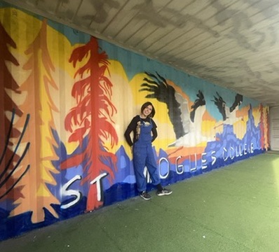 Aisling in front of a long colourful tunnel mural with trees and birds