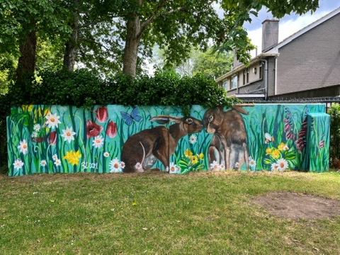 Two rabbits painted on a garden wall surrounded by wildflowers
